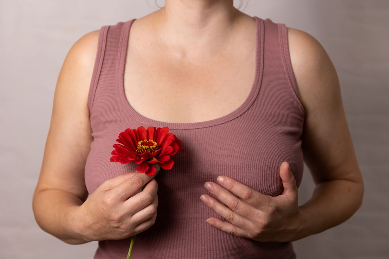 Mulher segundao uma rosa com uma mão e a outra sobreponto o seio para representar que há nódulo palpável na mama.