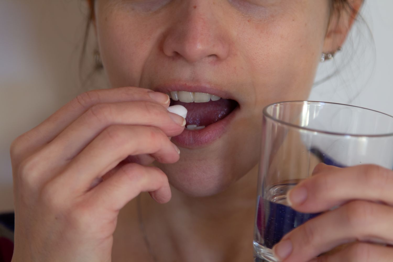 Mulher prestes a tomar comprimido branco com copo d’água, representando tratamento com tamoxifeno para câncer de mama.