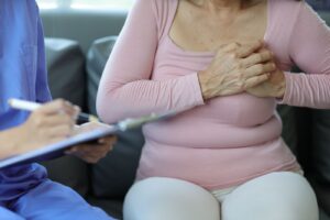 Mulher com mãos sobre a mama em ambiente médico, acompanhada de profissional de saúde, simbolizando avaliação de sintomas mamários.