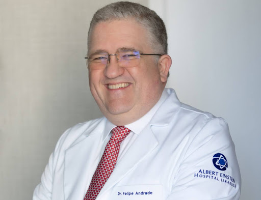 Dr. Felipe Andrade sorrindo, vestindo jaleco branco com gravata vermelha e logotipo do Hospital Israelita Albert Einstein.