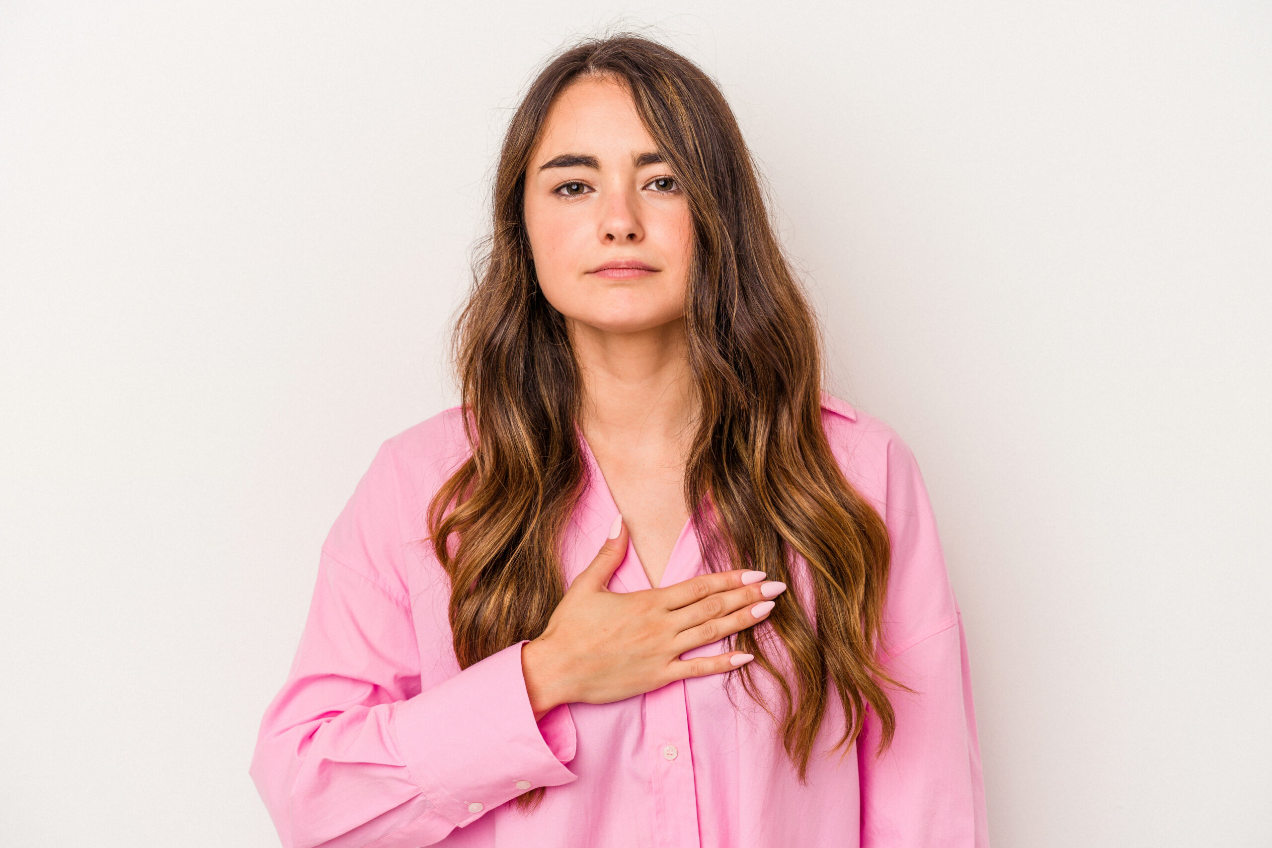Mulher jovem com a mão sobre a região do peito, representando atenção e cuidado com a saúde das mamas, em referência à importância de observar alterações na pele como covinhas ou afundamentos.