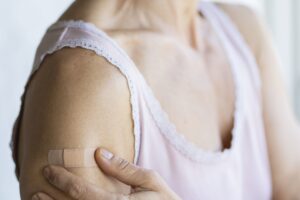 Mulher com curativo no braço após aplicação de medicamento injetável relacionado ao tratamento oncológico.