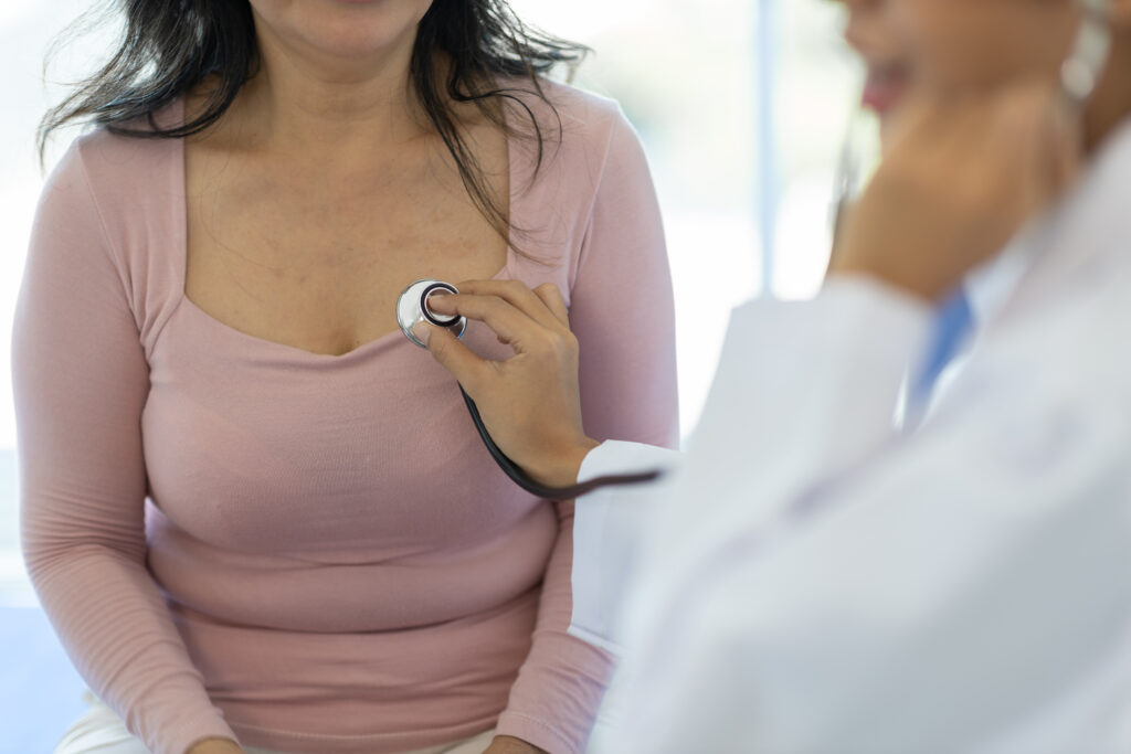 Médica examinando região mamária de paciente com estetoscópio durante consulta clínica.