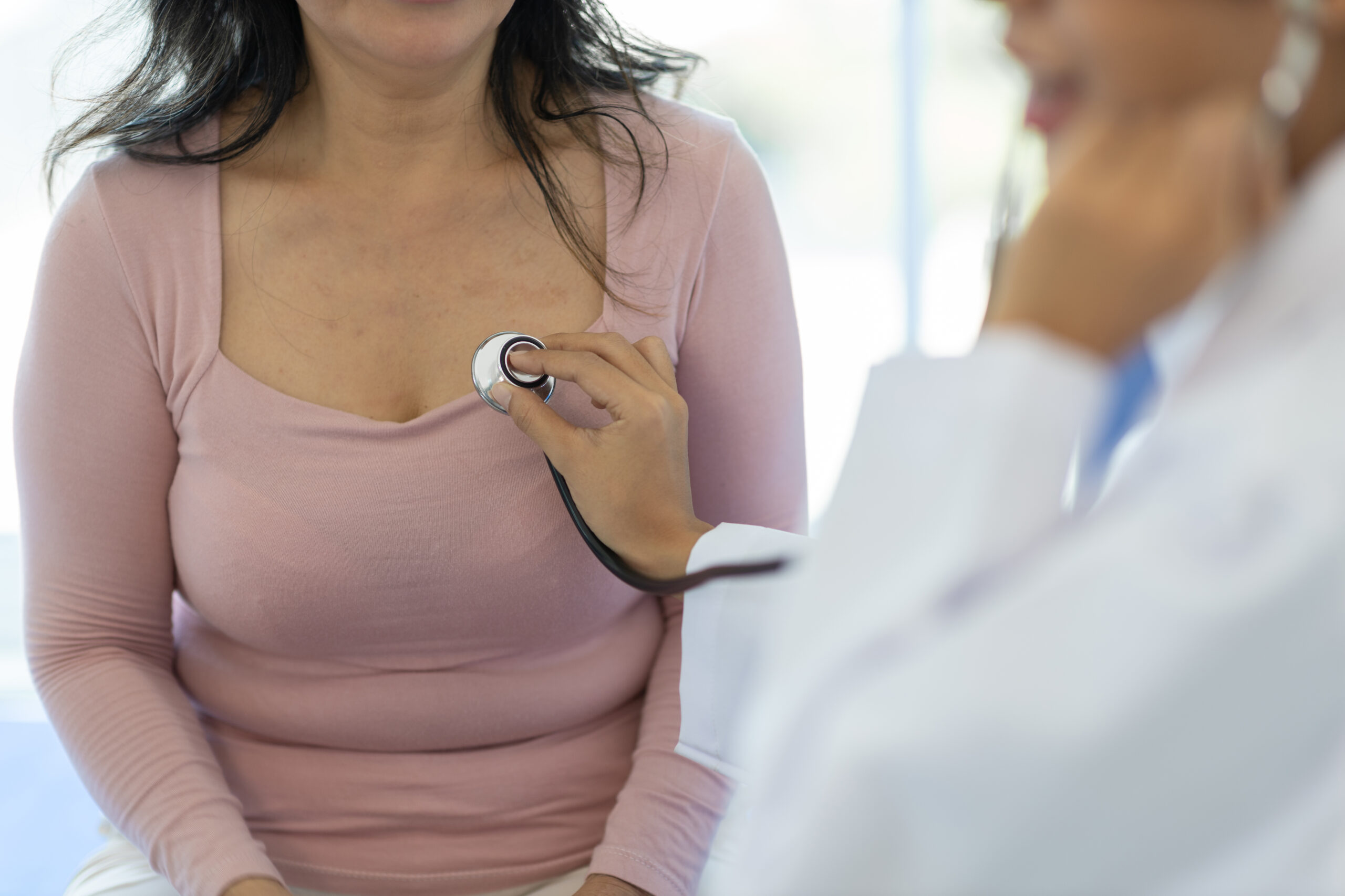 Médica examinando região mamária de paciente com estetoscópio durante consulta clínica.