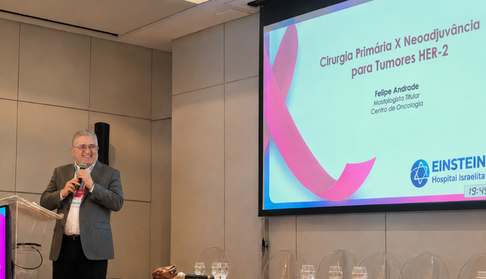 Dr. Felipe Andrade, mastologista, apresenta palestra sobre cirurgia primária versus neoadjuvância para tumores HER-2 em evento de mastologia.