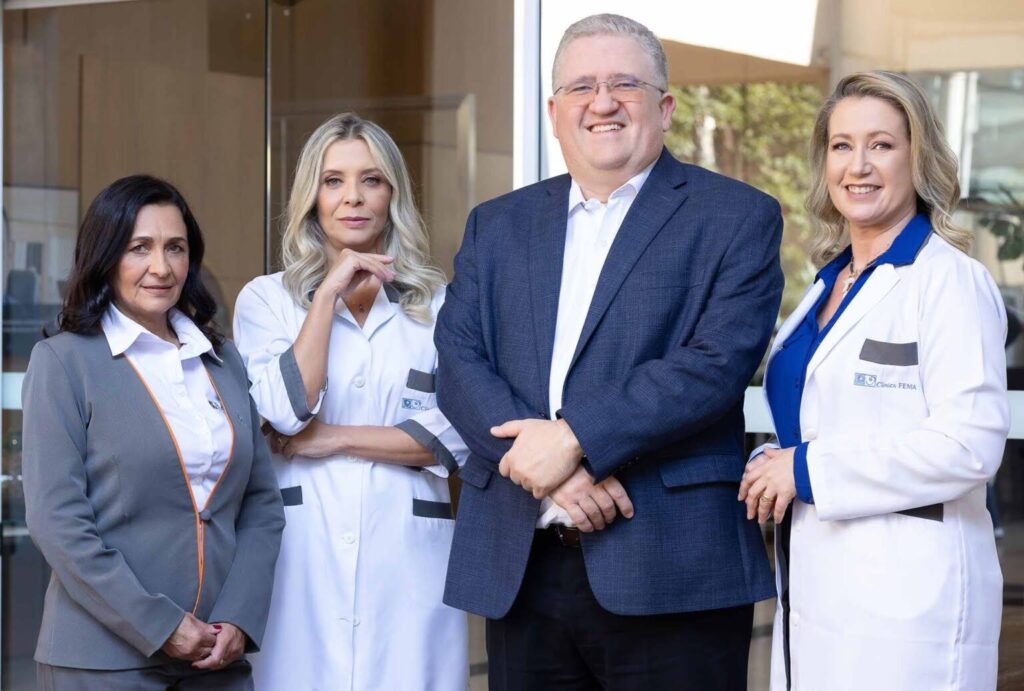 Equipe da Clínica FEMA reunida em frente à entrada da clínica, composta por três profissionais da saúde e um médico mastologista, representando atendimento especializado e abordagem multidisciplinar no tratamento do câncer de mama HER2 positivo.