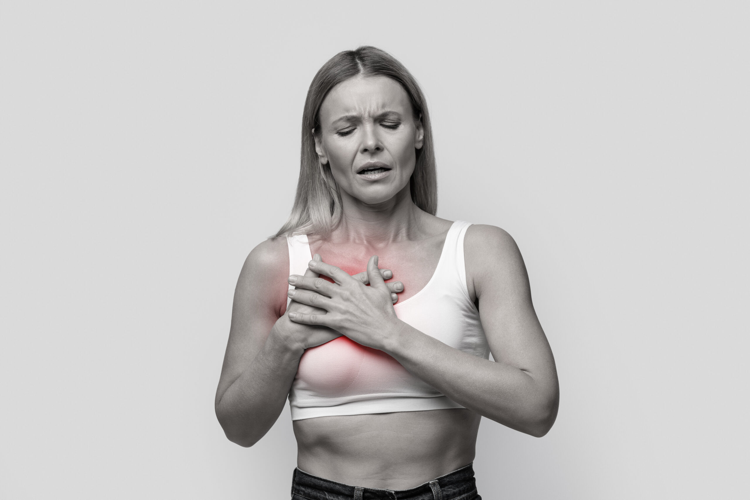 Mulher com expressão de dor segura o peito com as duas mãos, com área destacada em vermelho indicando sensibilidade ou desconforto na mama.