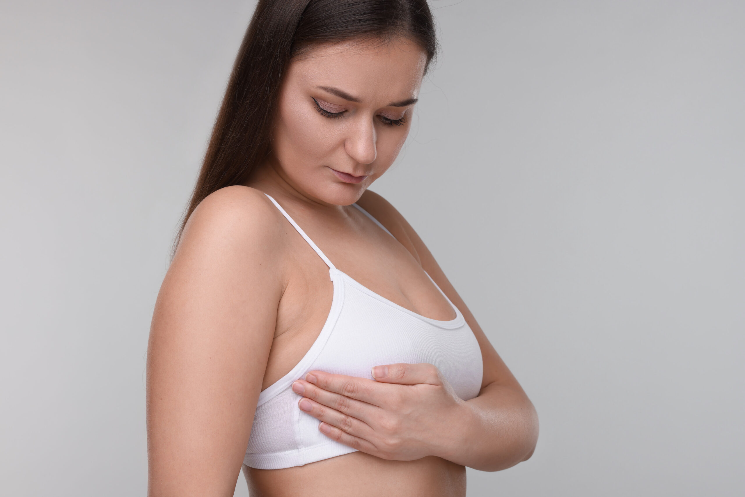 Mulher examina uma das mamas com a mão, observando possível inchaço unilateral.