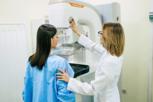 Exame de mamografia sendo realizado com posicionamento da paciente por profissional de saúde em clínica médica.
