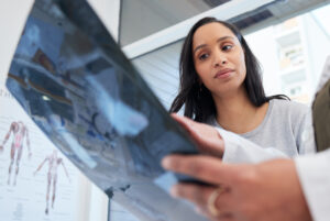 Mulher observa exame de imagem ao lado de profissional de saúde em consultório, representando avaliação mamária inconclusiva e necessidade de exames complementares.