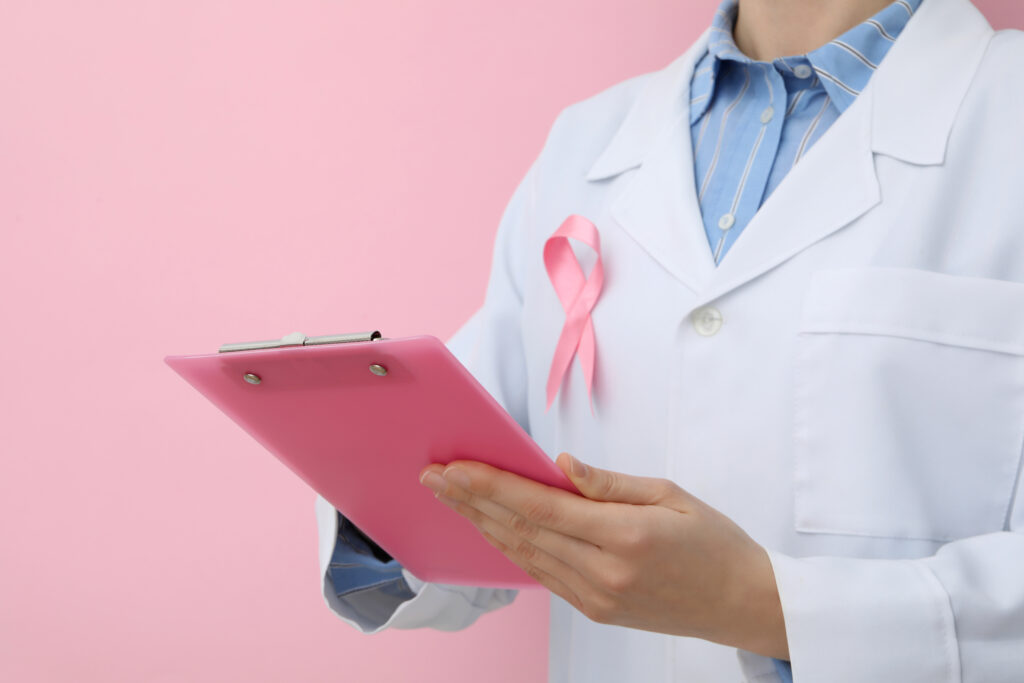 Médica mastologista de jaleco branco com laço rosa segurando prancheta durante consulta sobre resultado de mamografia com classificação BI-RADS® 4A.
