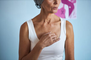 Mulher usando lenço na cabeça toca a região do peito durante tratamento oncológico, representando atenção a alterações mamárias e investigação de possíveis sinais de câncer de mama.